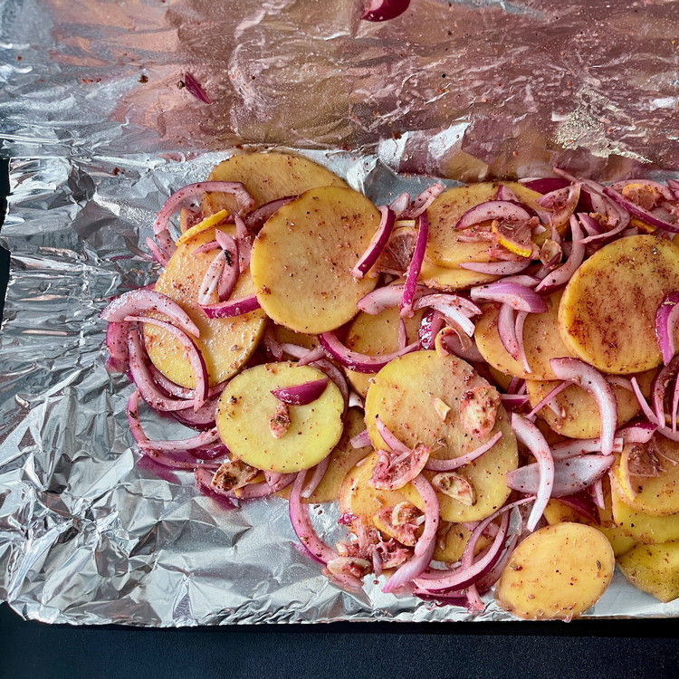Image of Arrange the potato mixture onto half of one of the prepared pieces of foil.Spread the layers of potatoes so they are no more than 2 potatoes deep to help them cook more evenly.